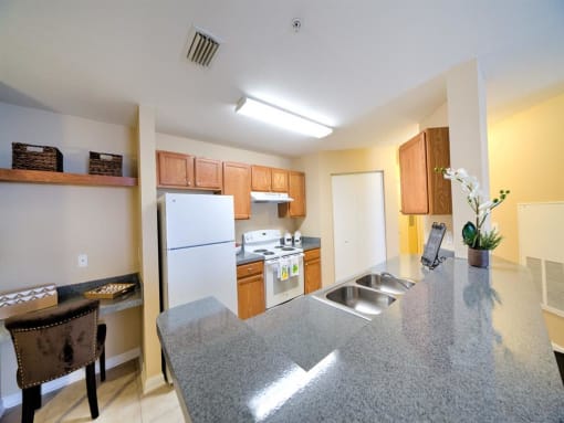 Kitchen with white appliances, breakfast bar, desk area with floating shelves, and tile flooring