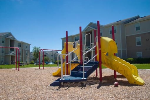 Blue Red and Yellow Playground on Mulch with Building Exteriors in the Background
