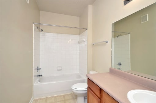 Vacant apartment bathroom with beige walls and linoleum flooring. Shower tub combo in the background and toilet.
