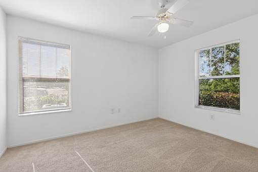 A room with a ceiling fan and two windows.