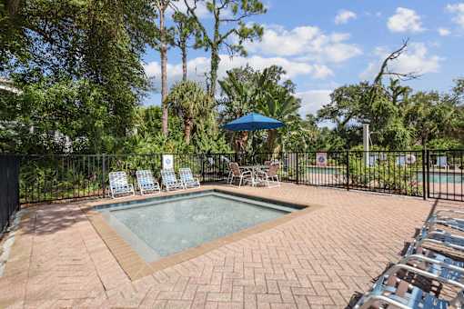 A pool surrounded by chairs and trees.