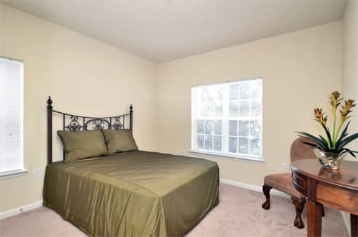 Apartment bedroom with double bed and comforter. The room features a table and chair as well.