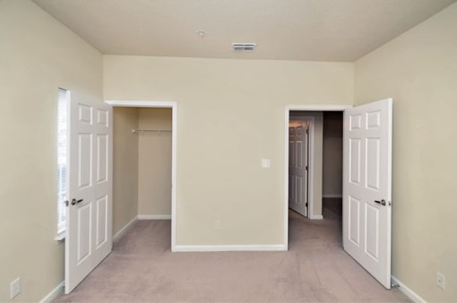 Vacant bedroom with tan carpet. beige walls, and a closet on the back wall. The entry door is to the right of the closet.