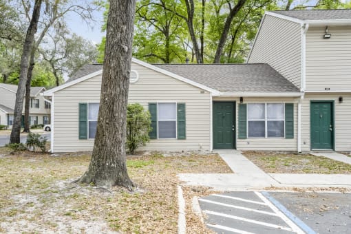 a white house with green doors and a large tree in the front yard