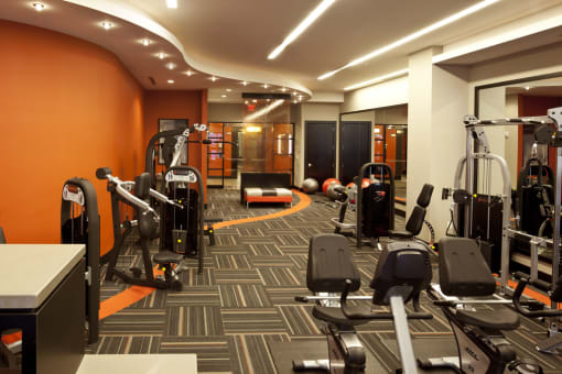 Fitness center with weighted equipment and full size mirrors against wall with orange accent colors