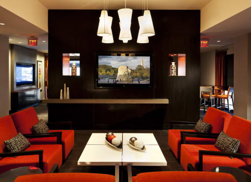 Clubroom seating area. Four orange accent chairs around white coffee table with tv in background