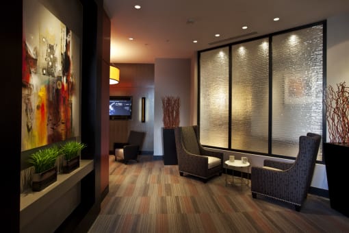 Clubroom seating area. Two grey accent chairs with coffee table. Tv and smaller seating area in background. Orange and wood accent colors.