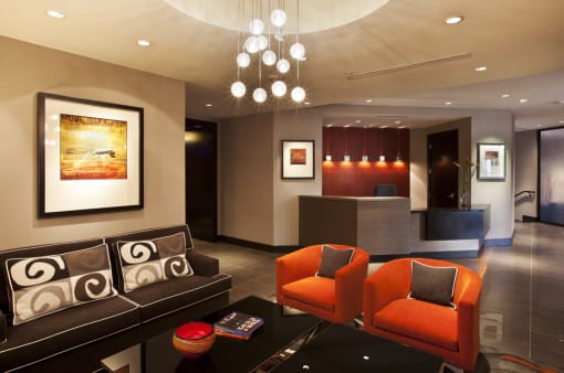 Clubroom seating with couch and two orange accent chairs with coffee table. Leasing desk and office in background.