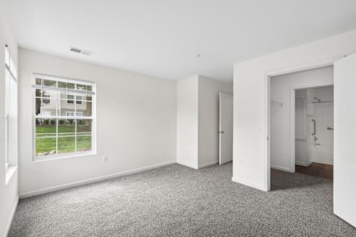 A large empty room with a window and carpeted floor.
