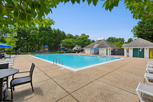 A pool surrounded by a patio with chairs and a table.
