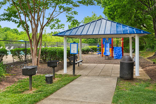 A gazebo with a blue roof is surrounded by trees and has a sign in front of it.