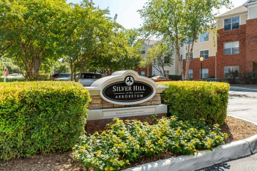 Community Entrance Sign on Parking Lot Median in Front of Tree Line with Shrubs