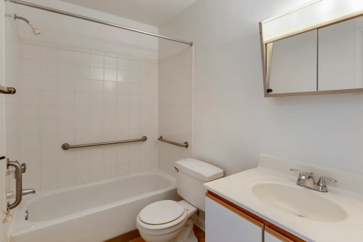 Bathroom with White Cabinets White Counters and White Bathtub and Shower with Handrails