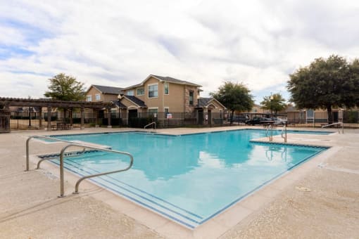Swimming pool with tanning deck, green trees, and view of the clubhouse in the background
