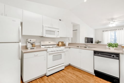 Virtually staged kitchen with white appliances, wood flooring, gas stove, ceiling fan, wall mounted television, dishwasher
