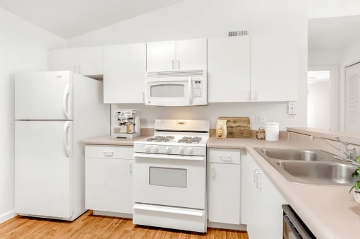 Virtually staged kitchen with white appliances, wood flooring, gas stove