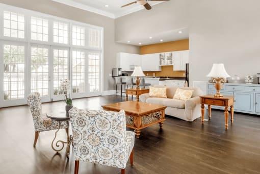 Clubhouse interior with hard wood flooring, couch, fabric seating, coffee table, ceiling fans, kitchen, large windows and doors
