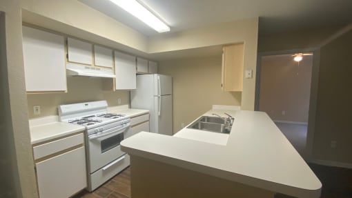 Kitchen featuring white cabinets, white appliances, white countertop, gas stove, and fluorescent tube lighting