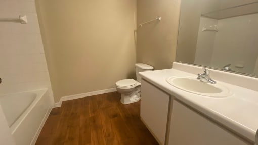 Bathroom featuring, wood flooring white countertop vanity , toilet, and tub with tile back splash, towel bar, and mirror