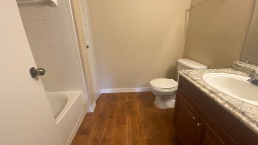 Bathroom with wood floors, granite vinyl  countertop, tub with tile back splash, and toilet