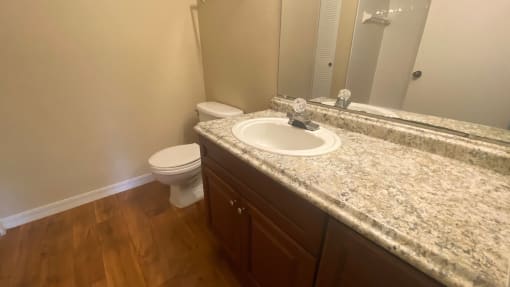 Bathroom with wood floors, extended granite vinyl countertop, mirror, and toilet