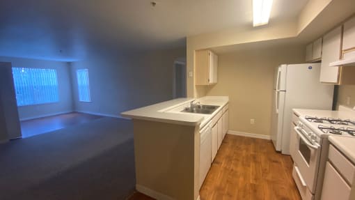 Kitchen featuring white cabinets, white appliances, white countertop, gas stove, view of living room, view of two widows in living room