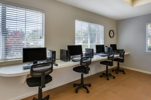 Clubhouse business center with computers, chairs, desk, and large windows for natural lighting