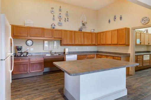 Clubhouse Kitchen with kitchen island, hardwood style floors, wooden cabinetry, and a white refrigerator