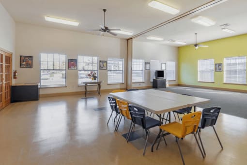 Activity room with tables and chairs, ceiling fan, and tile flooring, sliding partition and carpeted area and television