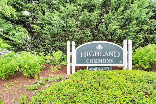 A sign for Highland Commons Apartments is surrounded by greenery.