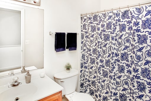 Virtually staged bathroom with blue accent towels, wood cabinets and white couters