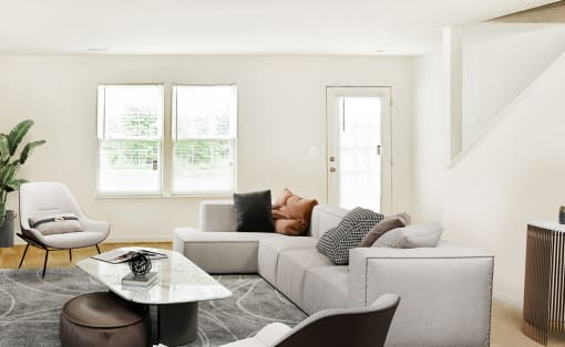 Virtually staged living room interior with grey couch, grey side chairs, and coffee table. Large window next to entry in background