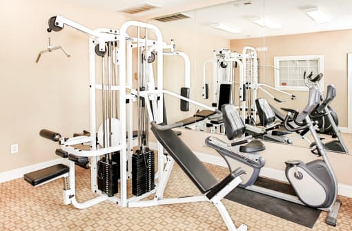 Fitness center with weighted equipment and full size mirrors against wall with orange accent colors