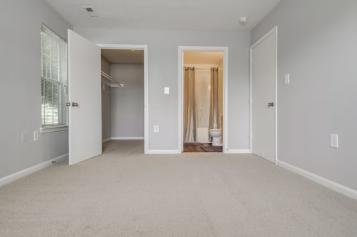Empty bedroom with carpet, closet, ensuite bathroom and window