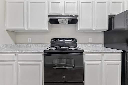 A black stove in a kitchen with white cabinets.
