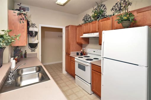 Apartment galley kitchen with brown cabinets, beige walls, and white appliances. Dining area is on the far side of the room.