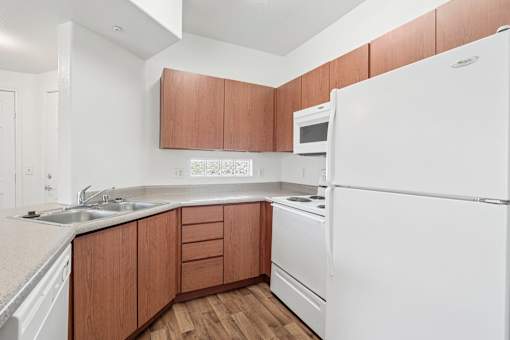 Compact kitchen with wood cabinetry and white appliances at Lake Pleasant Village Apartments, Peoria, Arizona