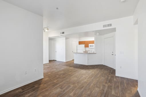 the living room and kitchen of an apartment with white walls and wood flooring