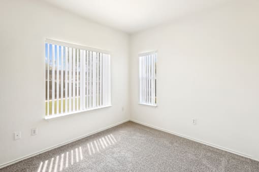 an empty room with two windows and a carpeted floor