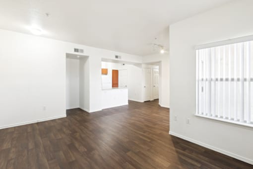 the living room and kitchen of an apartment with white walls and wood flooring