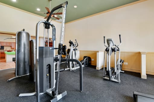 a gym with exercise machines and a kitchen in the background