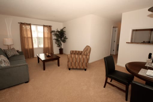 Spacious living room with carpet flooring, couch, coffee table, chair, dining room table with chairs, and large mirror with curtains