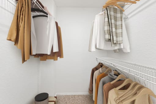 a walk in closet with clothes hanging on a rack and a small stool on the floor