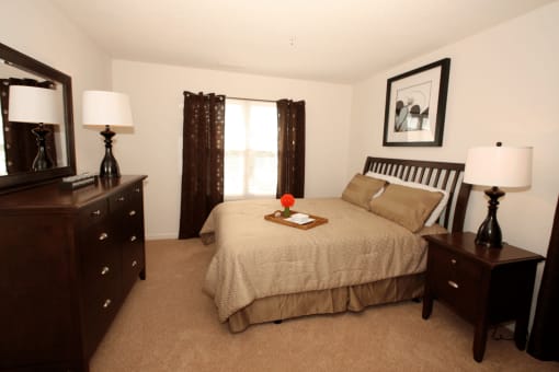 Bedroom with carpet flooring, dresser, bed, night stand, wall art, and large window with curtains