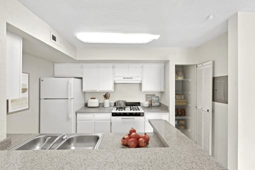 a kitchen with white cabinets and appliances and a counter with a bowl of fruit on it