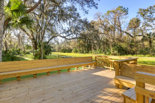 a large wooden deck with benches and trees in the background