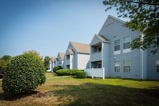 A row of houses with green lawns and trees in front.
