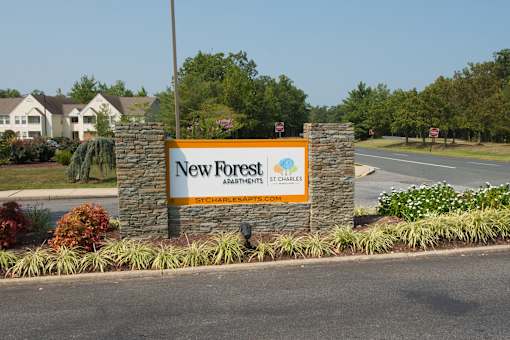 A sign for New Forest St. Charles Apartments is displayed in front of a road.