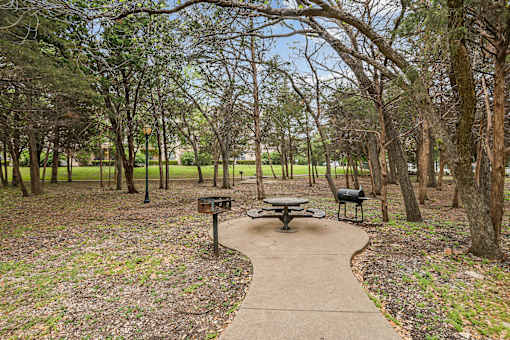 A picnic table sits in the middle of a park with a pathway leading to it.