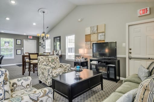 Clubhouse with arm chairs and coffee table. High top table with chairs. Television on an entertainment center.